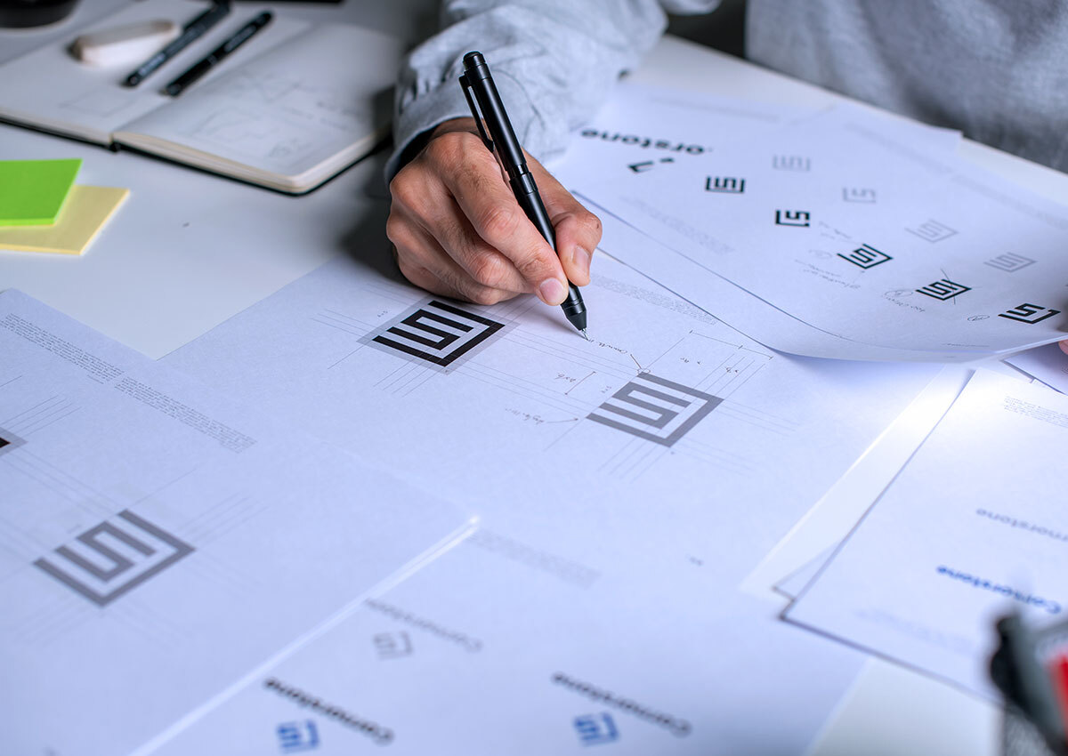 Close up of a man working on the visual identity for a brand. She is making notations on a logo mark.